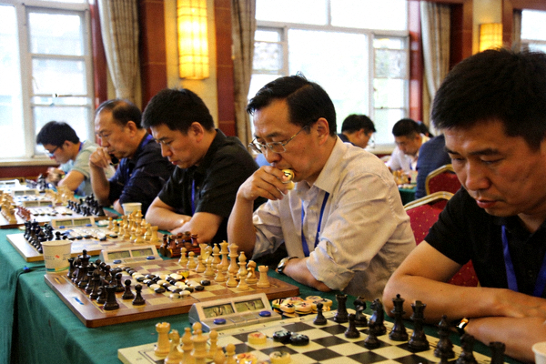智力运动会棋牌项目比赛现场，选手们围坐于长桌前专注对弈
